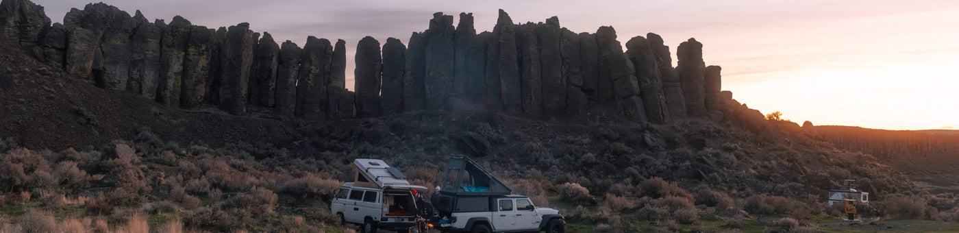 Two vehicles parked in a desert landscape with rock formations and sunset.