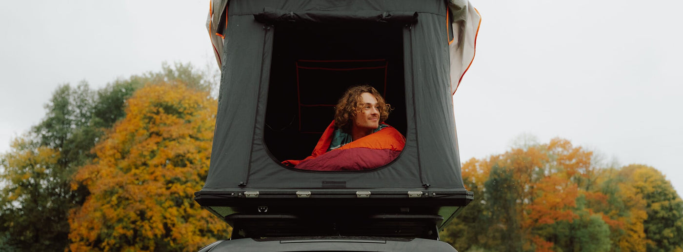 Person inside a rooftop tent with autumn trees in the background